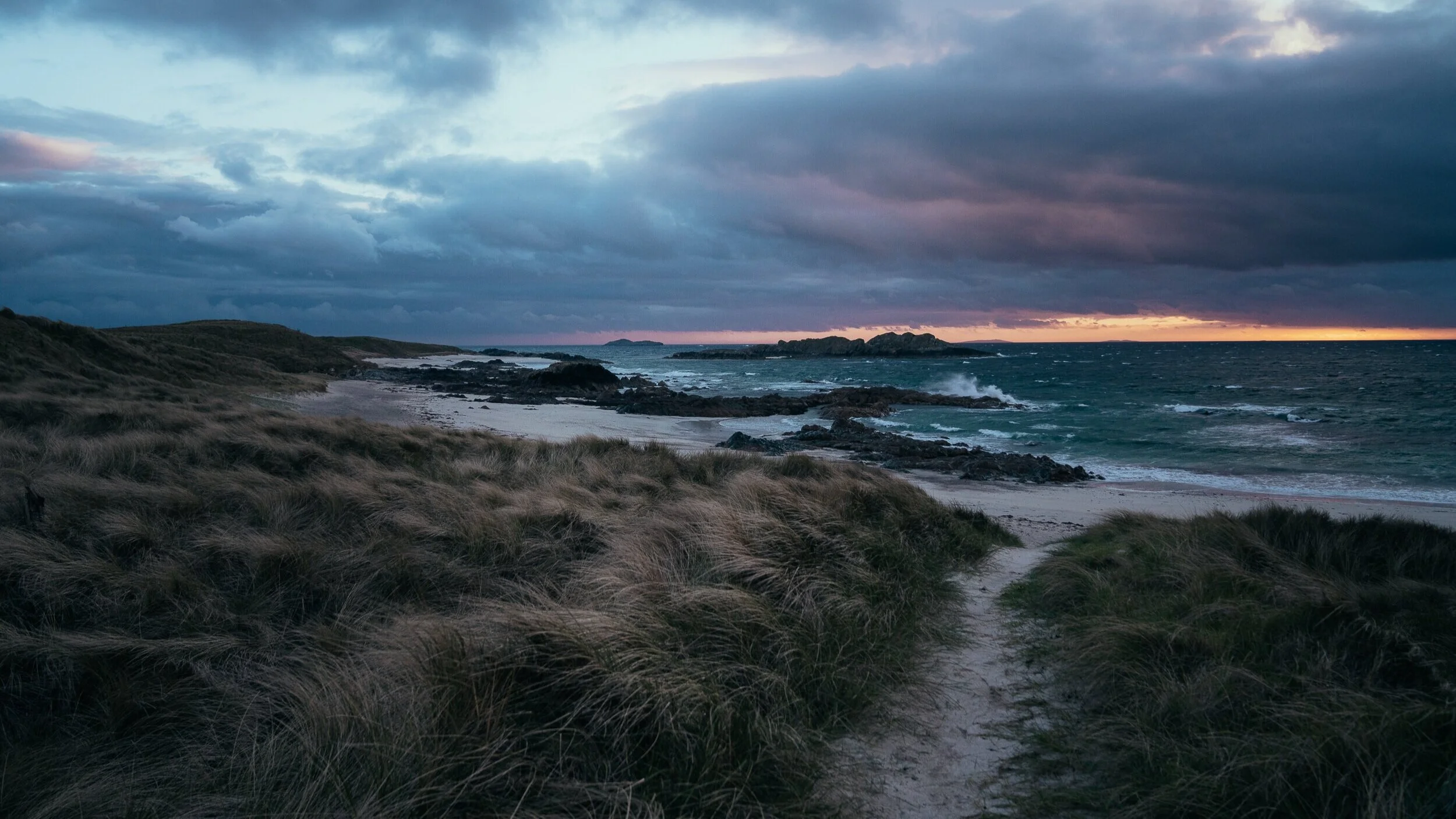 Twilight path through windswept dune grass toward the sea on Iona