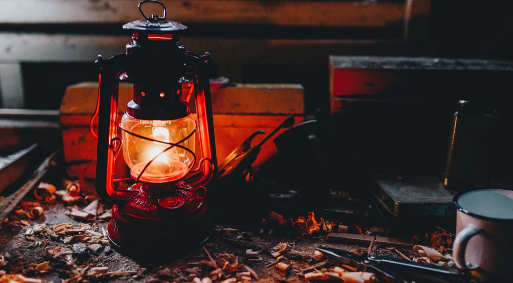 Hurricane lantern glowing on a workbench in the dark