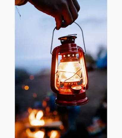 Hand holding a glowing hurricane lantern at dusk
